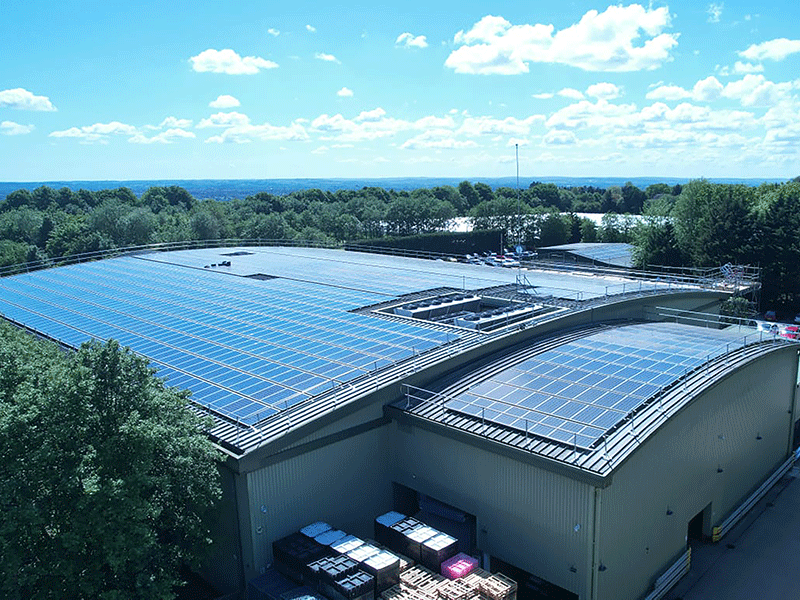 Fixed guardrail on a large industrial roof, with smaller one to the side. Both roofs are full of solar panels.