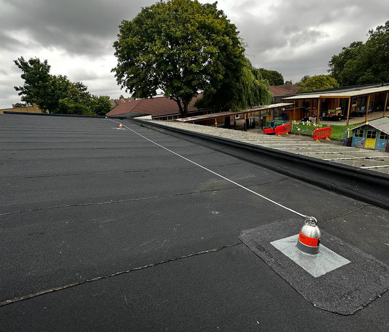 Lifeline system installed on a flat roof. There's a children's playground and tree in the background.