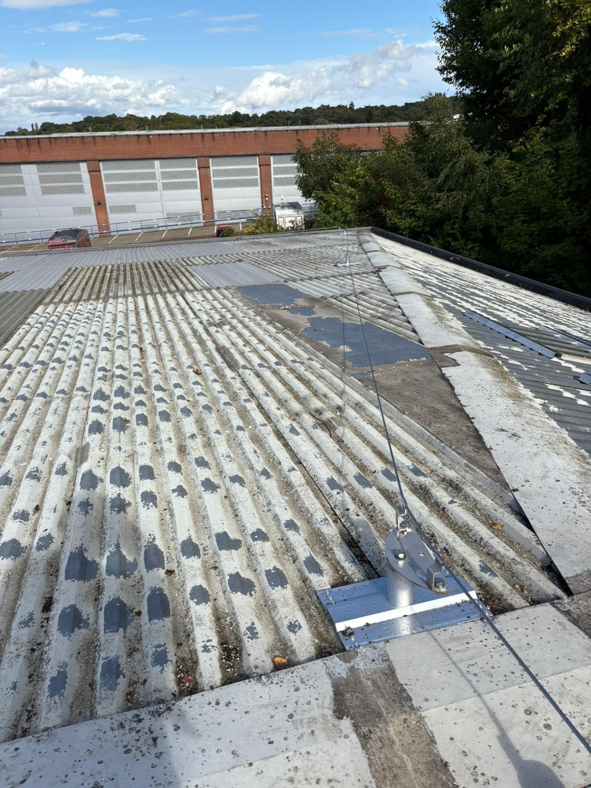Mansafe lifeline system installed on a corrugated industrial roof, with anchor point and safety cable running across weathered roofing near a commercial building.